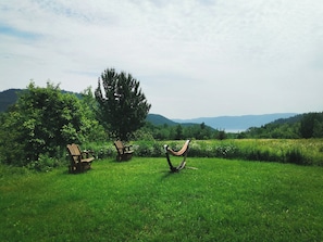 A grassy field with two wooden chairs and a hammock.