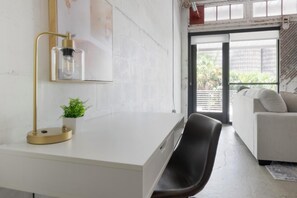 A modern room with a white desk, a black chair, a small potted plant, and a sofa. - Landing | Stunning 1BD, Rooftop Lounge, Gym (Jacksonville)