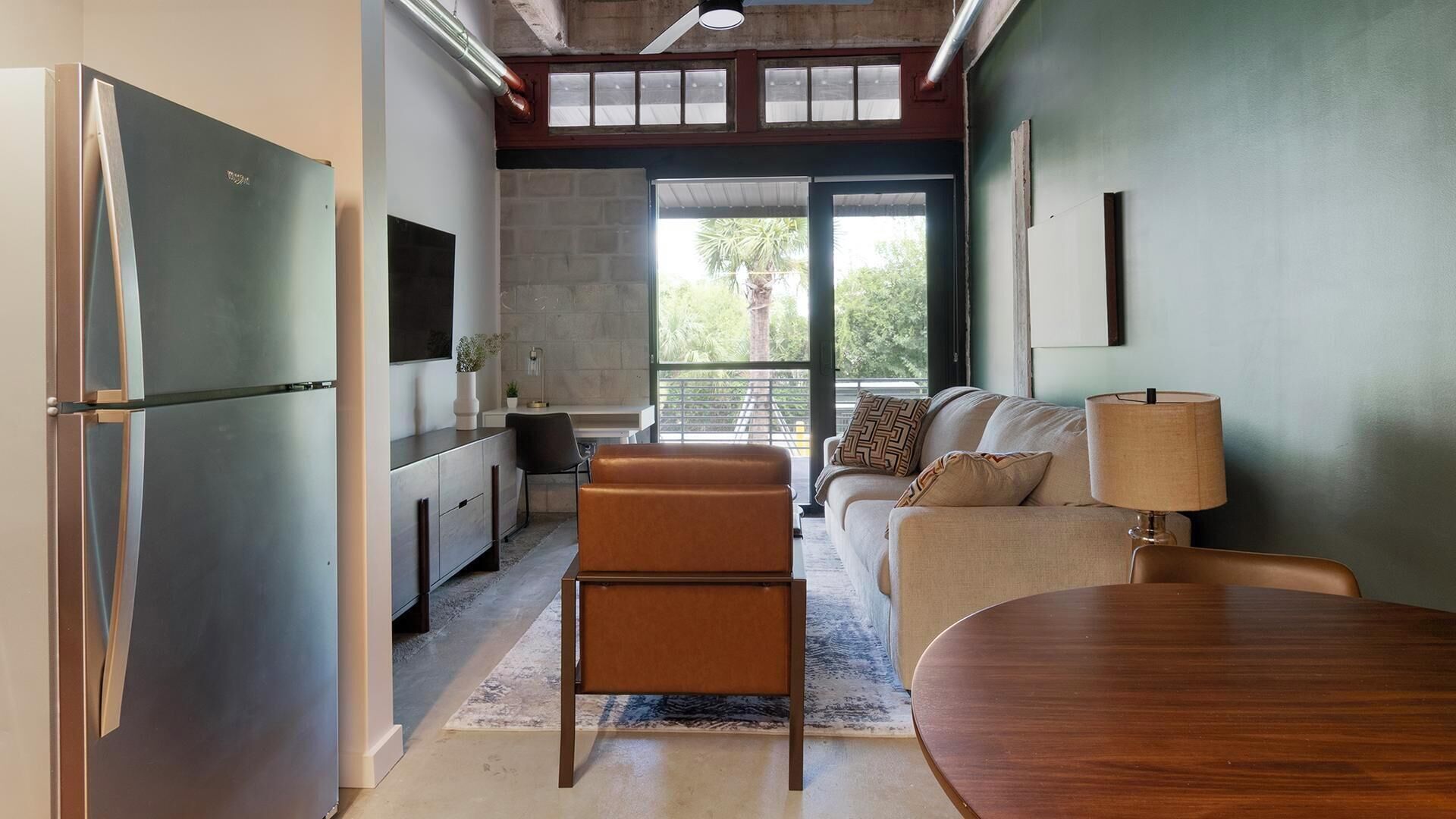 A modern kitchen with a built-in refrigerator, a dining area with a wooden table, and a seating area with a sofa and a lamp.