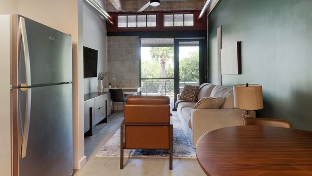 A modern kitchen with a built-in refrigerator, a dining area with a wooden table, and a seating area with a sofa and a lamp. - Landing | Amazing 1BD, Gym, Rooftop Lounge (Jacksonville)