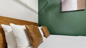 A bed with white bedding and two brown pillows, a wooden headboard, and a green wall with a painting. - Landing | Amazing 1BD, Gym, Rooftop Lounge (Jacksonville)