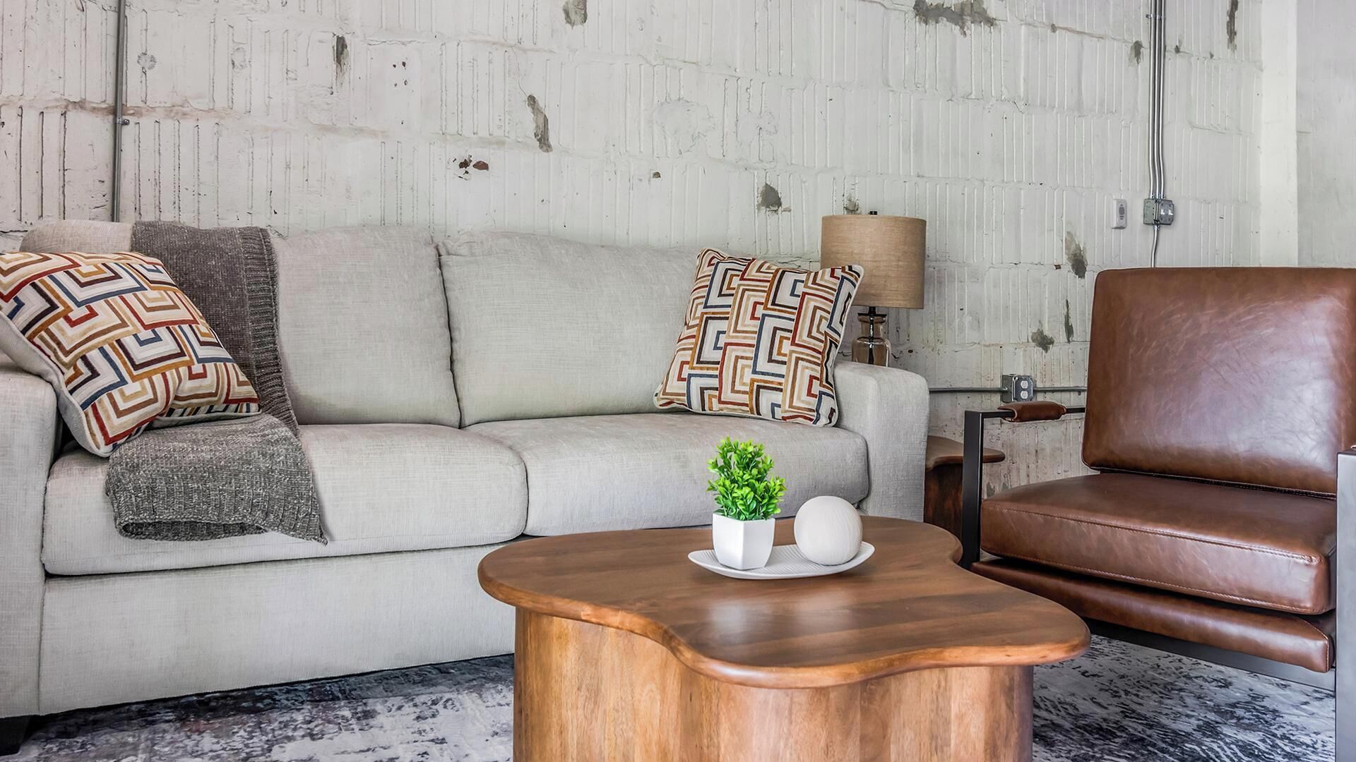 A living room with a sofa, a brown leather chair, a wooden coffee table with a plant, and patterned throw pillows.