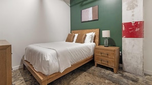 A bedroom with a wooden bed, white bedding, a nightstand with a lamp, and a green wall with a red and white section. - Landing | Spectacular 1BD, Rooftop Lounge, Gym (Jacksonville)