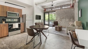 A modern kitchen with stainless steel appliances, a dining area with a round table and chairs, and a view of the outdoors through large windows. - Landing | Spectacular 1BD, Rooftop Lounge, Gym (Jacksonville)