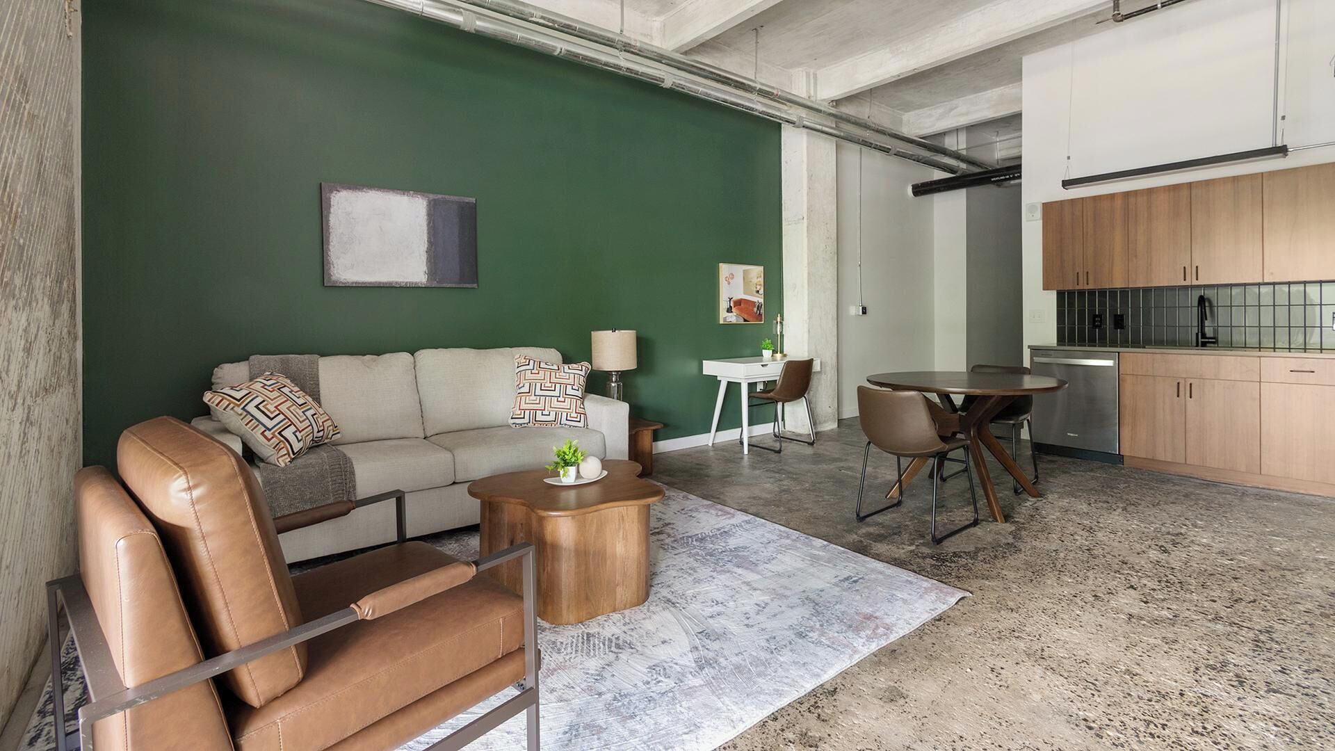 A modern living space with a green accent wall, a sofa, a coffee table, a dining area with chairs, and a kitchen with wooden cabinets.