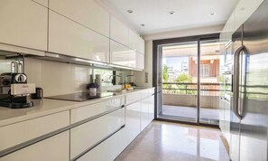 Eine moderne Küche mit integrierter Espressomaschine, einer Schiebeglastür zum Balkon und einem Edelstahlkühlschrank.