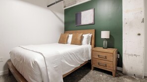 A bedroom with a bed, a nightstand, a lamp, and a painting on the wall. - Landing | Beautiful 1BD, Gym, Rooftop Lounge (Jacksonville)