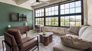 A room with a large window, a flat-screen TV, a sofa, a chair, and a small table. - Landing | Beautiful 1BD, Gym, Rooftop Lounge (Jacksonville)