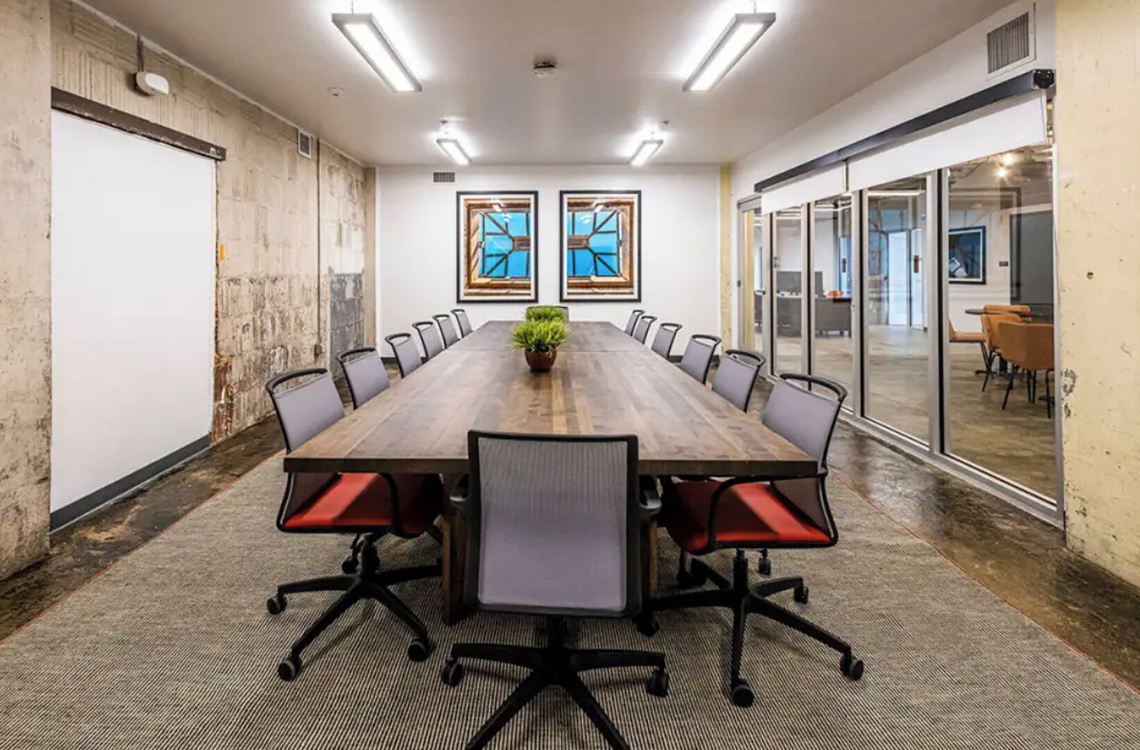 Une salle de conférence avec une longue table, des chaises et deux œuvres d’art encadrées accrochées au mur.