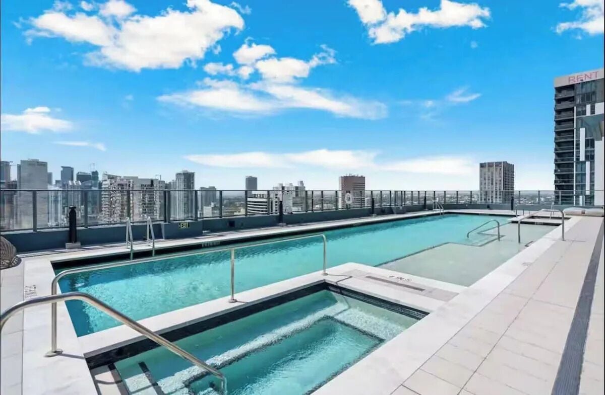 Una piscina en la azotea con vistas a un horizonte urbano, rodeada por una cerca de metal.