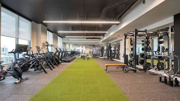 Academia com esteiras, máquinas de peso e uma pista com carpete verde.
