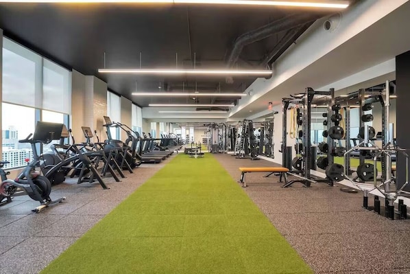 A gym with treadmills, weight machines, and a green carpeted path. - Miami Luxe Suites (Miami)