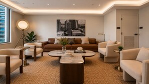 A modern living room with a brown leather sofa, beige armchairs, a round coffee table, and a cityscape painting on the wall. - Miami Luxe Suites (Miami)