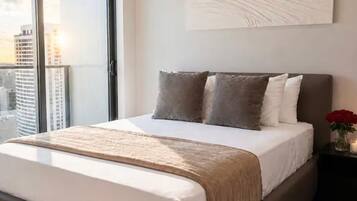 Un dormitorio moderno con una cama grande, vistas a la ciudad y una obra de arte minimalista en la pared.