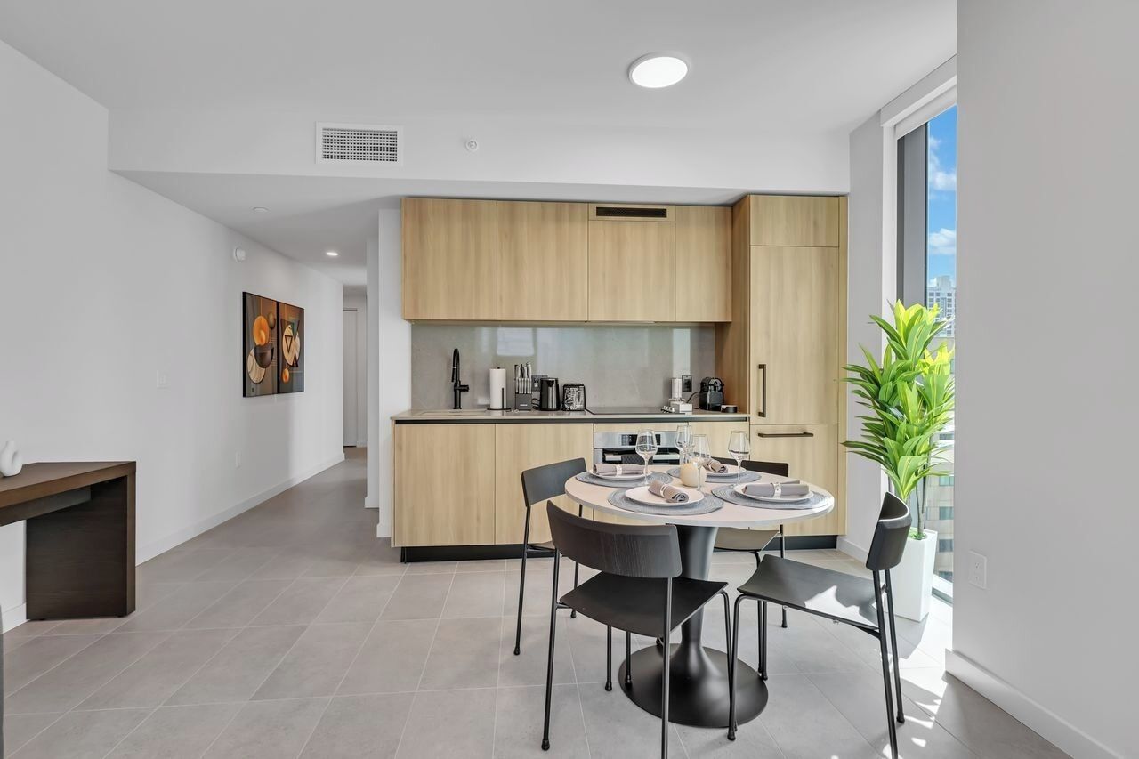 A modern kitchen with a dining area, featuring a round table with chairs, a built-in oven, and a large window with a view.