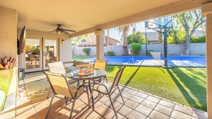 A patio with a table and chairs, a ceiling fan, and a view of a backyard with a basketball court. - Luxury 5BR Retreat, Heated Pool, Spa, Sport Court, Putting Green & Game Rooms (Scottsdale)