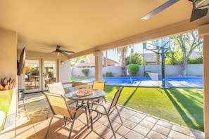 A patio with a table and chairs, a ceiling fan, and a view of a backyard with a basketball court. - Luxury 5BR Retreat, Heated Pool, Spa, Sport Court, Putting Green & Game Rooms (Scottsdale)