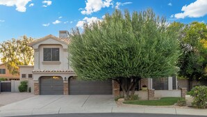 A residential house with a garage, a driveway, and a well-maintained lawn. - Luxury 5BR Retreat, Heated Pool, Spa, Sport Court, Putting Green & Game Rooms (Scottsdale)