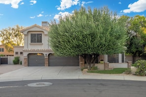A residential house with a garage, a driveway, and a well-maintained lawn. - Luxury 5BR Retreat, Heated Pool, Spa, Sport Court, Putting Green & Game Rooms (Scottsdale)