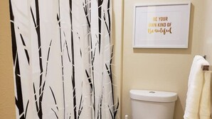 A bathroom with a toilet, a roll of toilet paper, a towel rack with a towel, and a wall-mounted sign.