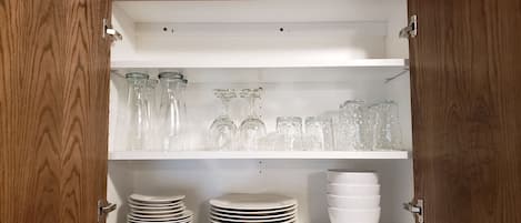 A kitchen cabinet with shelves holding glassware and white dishes.