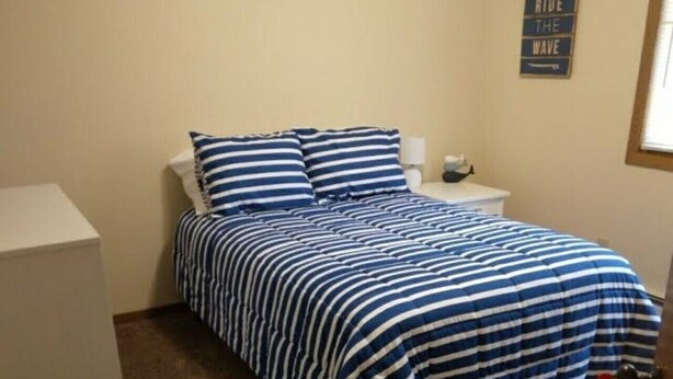 A bedroom with a bed, a nightstand, a lamp, and a wall sign.
