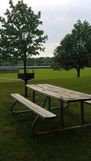 Ein Picknicktisch mit Bänken in einer grünen Parkanlage mit Bäumen.