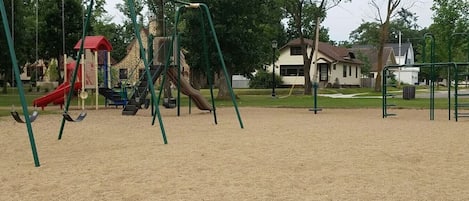 A playground with swings and slides, surrounded by trees and houses.