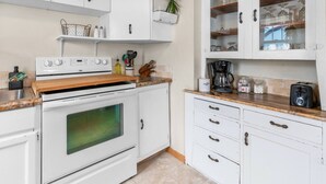 Una cocina con gabinetes blancos, estufa, cafetera y tostadora.