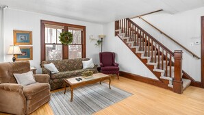 Una sala de estar con un sofá, sillones, una mesa de centro, una escalera y una ventana adornada con un adorno navideño.
