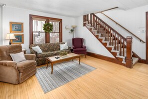 A living room with a sofa, armchairs, a coffee table, a staircase, and a window with a wreath. - KING bed home North of Downtown St. Cloud (St. Cloud)