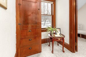 Ein Eckzimmer mit einem Holzschrank, einem kleinen Tisch mit Pflanze und einem Stuhl.