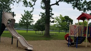 Un parque infantil con tobogán y estructuras para escalar, rodeado de árboles y una mesa de picnic.