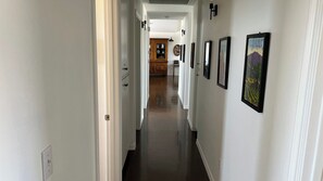 A hallway with framed artwork on the walls, a wooden cabinet in the background, and a door on the left. - Top of the Hill by Avantstay Vineyard Views + Fire Pit 1 Min to Wine Trail (San Miguel)