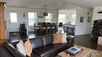 A spacious living room with a dark leather sofa, a dining area with wooden chairs, and a wine rack.