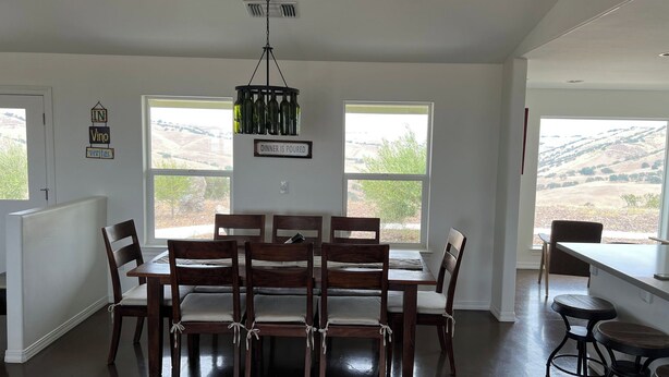 A dining area with a table and chairs, two windows with a view, and a chandelier. - Top of the Hill by Avantstay Vineyard Views + Fire Pit 1 Min to Wine Trail (San Miguel)