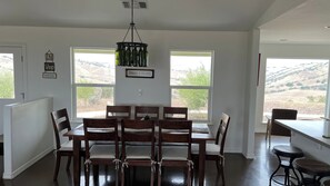 A dining area with a table and chairs, two windows with a view, and a chandelier.