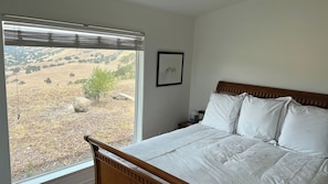 A bedroom with a bed, a window with blinds, a framed picture on the wall, and a view of a hilly landscape. - Top of the Hill by Avantstay Vineyard Views + Fire Pit 1 Min to Wine Trail (San Miguel)