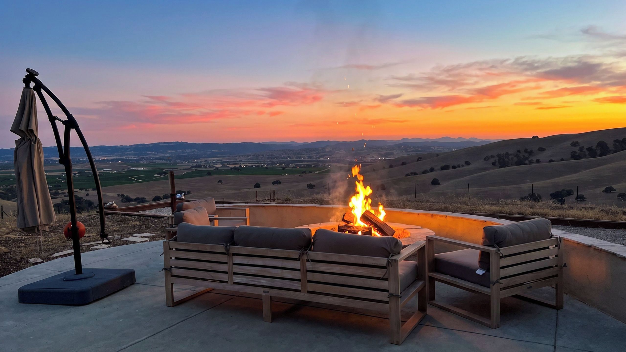 Un área de estar al aire libre con una chimenea, un telescopio y vistas al campo al atardecer.