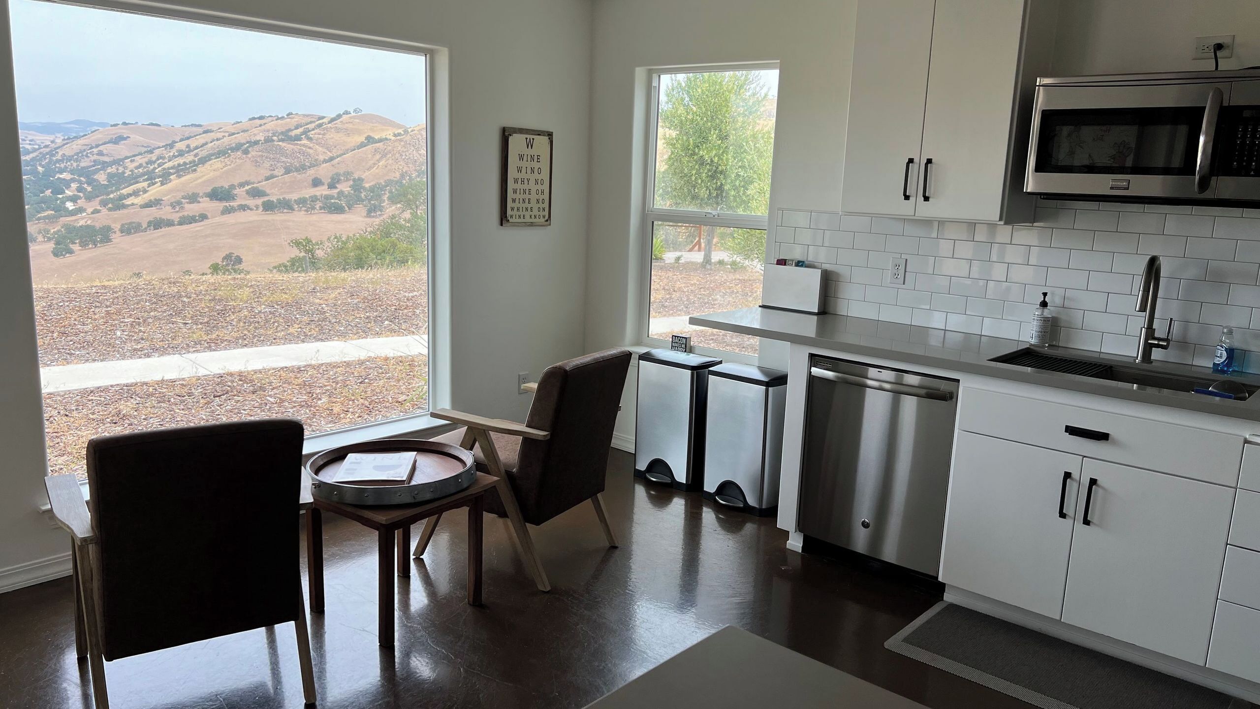 Una cocina moderna con vistas a colinas ondulantes, un comedor con mesa y sillas, y un microondas sobre el fregadero.