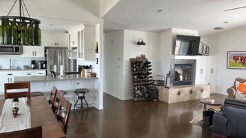 A modern kitchen with stainless steel appliances, a dining area with a wooden table and chairs, and a living room with a fireplace and seating.