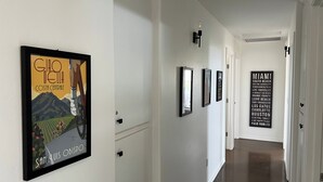 A hallway with framed artwork on the walls, a door at the end, and a light fixture. - Top of the Hill by Avantstay Vineyard Views + Fire Pit 1 Min to Wine Trail (San Miguel)