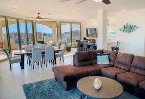 A modern living room with a brown leather sofa, a round coffee table, and a dining area with chairs and a table.