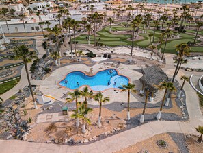 Vista aérea de un resort con piscina, palmeras y un campo de golf.