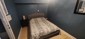 A bedroom with a bed, a nightstand, and a wall-mounted light fixture.