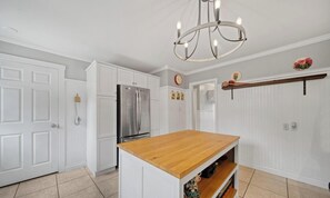 A kitchen with white cabinetry, a stainless steel refrigerator, a wooden island, and a chandelier. - 5 bedroom house with hot tub in a quiet street (Sooke)
