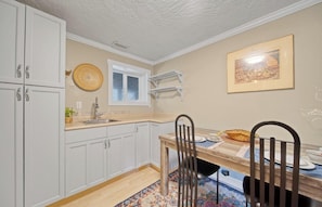 A kitchen with white cabinets, a wooden dining table, and a patterned rug.