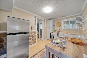 A modern kitchen with a refrigerator, dining table, chairs, and a stone accent wall. - 5 bedroom house with hot tub in a quiet street (Sooke)