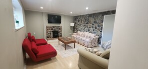 A living room with a stone wall, a fireplace, a red sofa, a beige sofa, and a wooden coffee table. - 5 bedroom house with hot tub in a quiet street (Sooke)