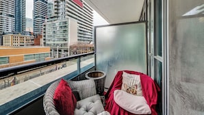 A balcony with a view of tall buildings, a wicker chair, a cushion, and a red cloth. - 🌿|| Cozy+Stylish Suite ||🍄 PRIME Entertainment District @ Spadina & King West! (Toronto)